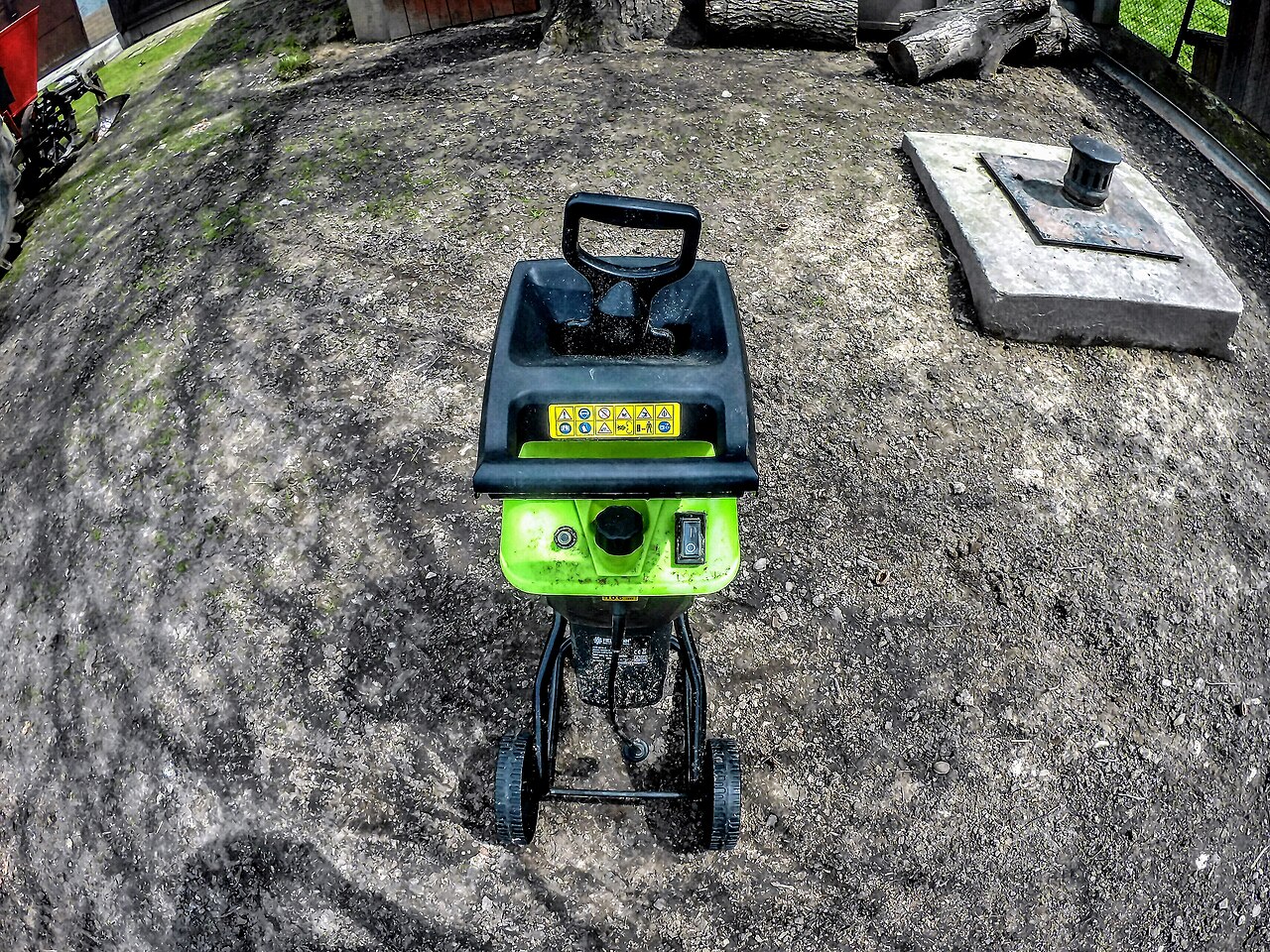 Broyeur électrique de jardin vert et noir, avec sa trémie et son piètement sur roues.