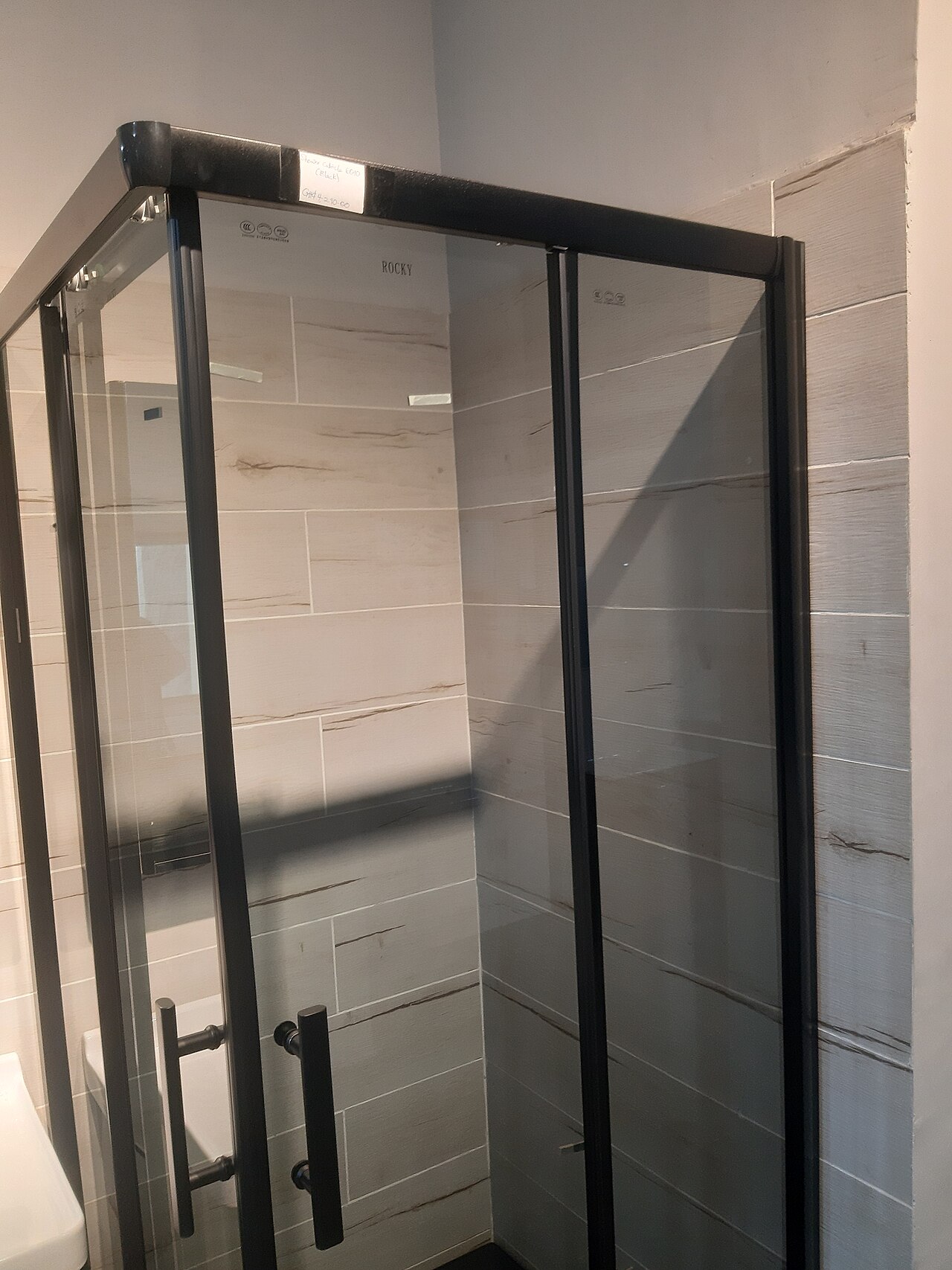 Cabine de douche vitrée installée devant un mur carrelé.
