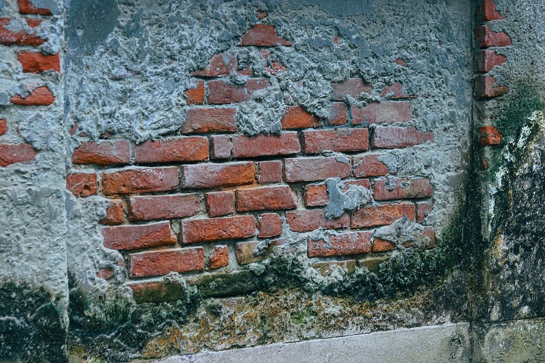 Enduit gris décollé laissant apparaître les briques d’un mur ancien