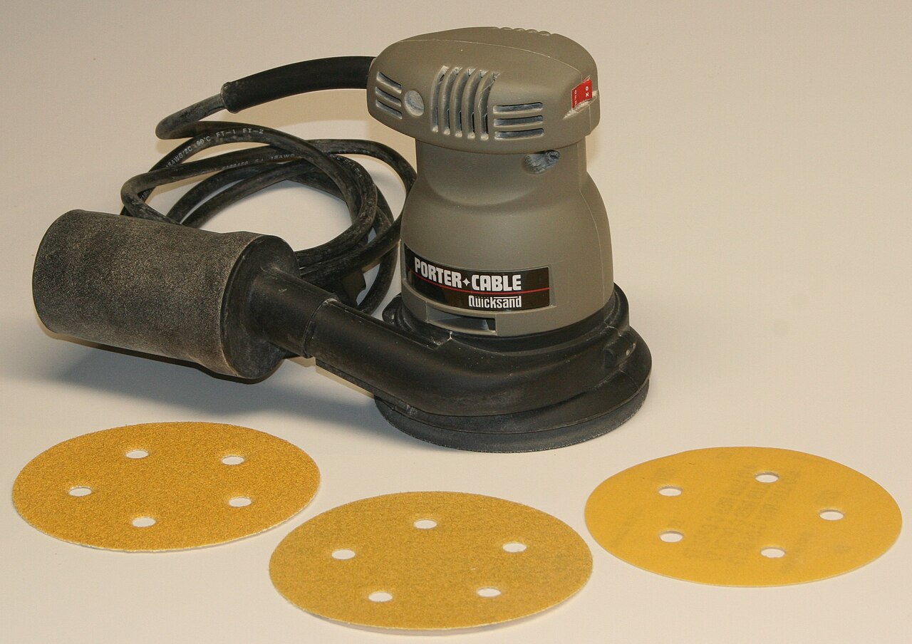 Ponceuse excentrique à plateau rond et sac à poussière, avec trois disques abrasifs perforés.